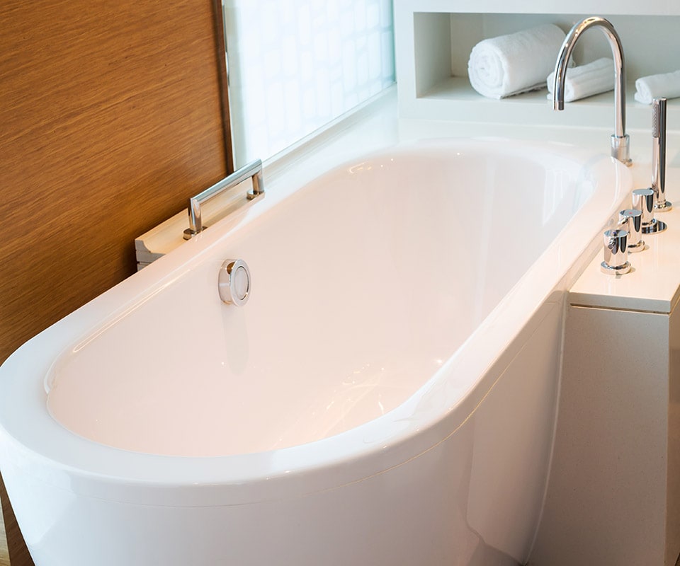 A beautiful and durable deep tub in white, with chrome fixtures, in a bright, richly paneled bathroom. Choose Hiester Construction foir bathroom remodeling and transform your space.