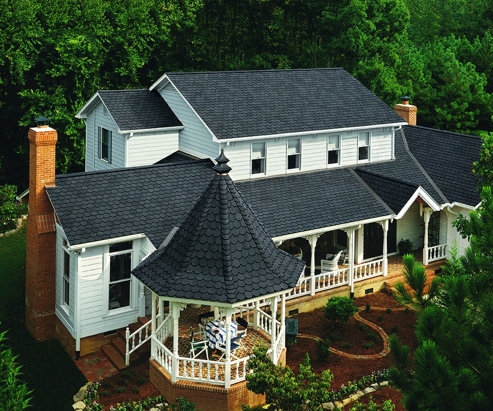 A white house with high quality roof of black Certainteed shingles. The property includes a shingled gazebo, landscaping and beautiful woods.